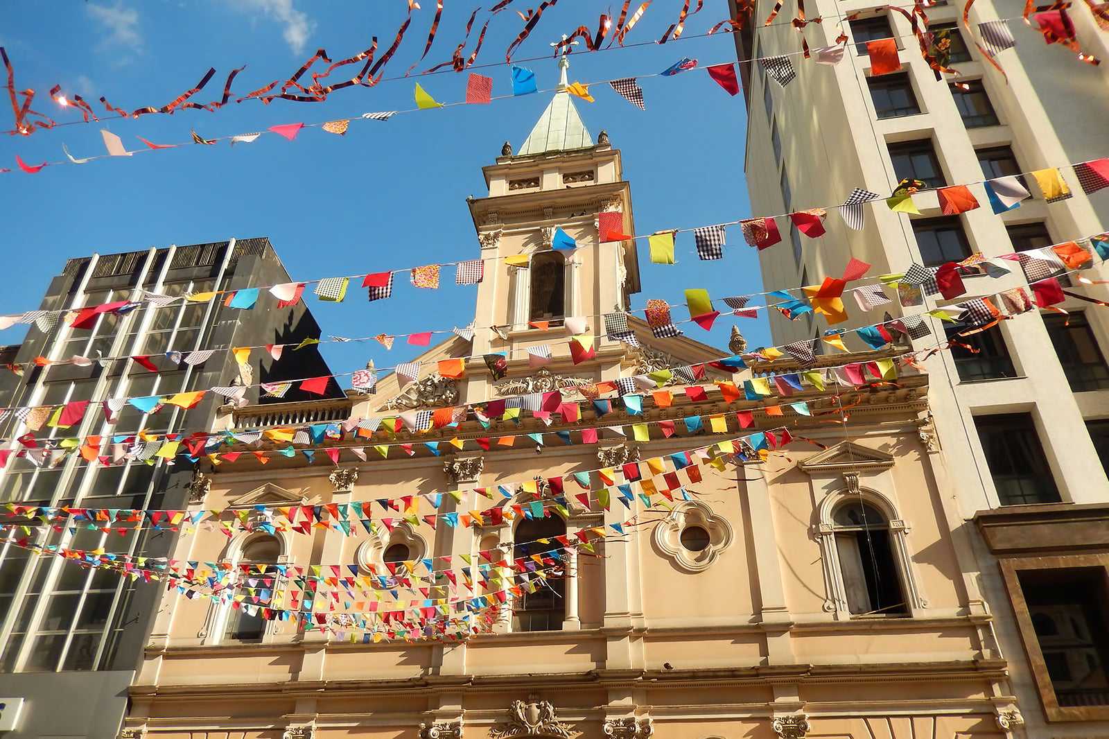 Festa junina em São Paulo com bandeirinhas coloridas e igreja histórica ao fundo durante o dia