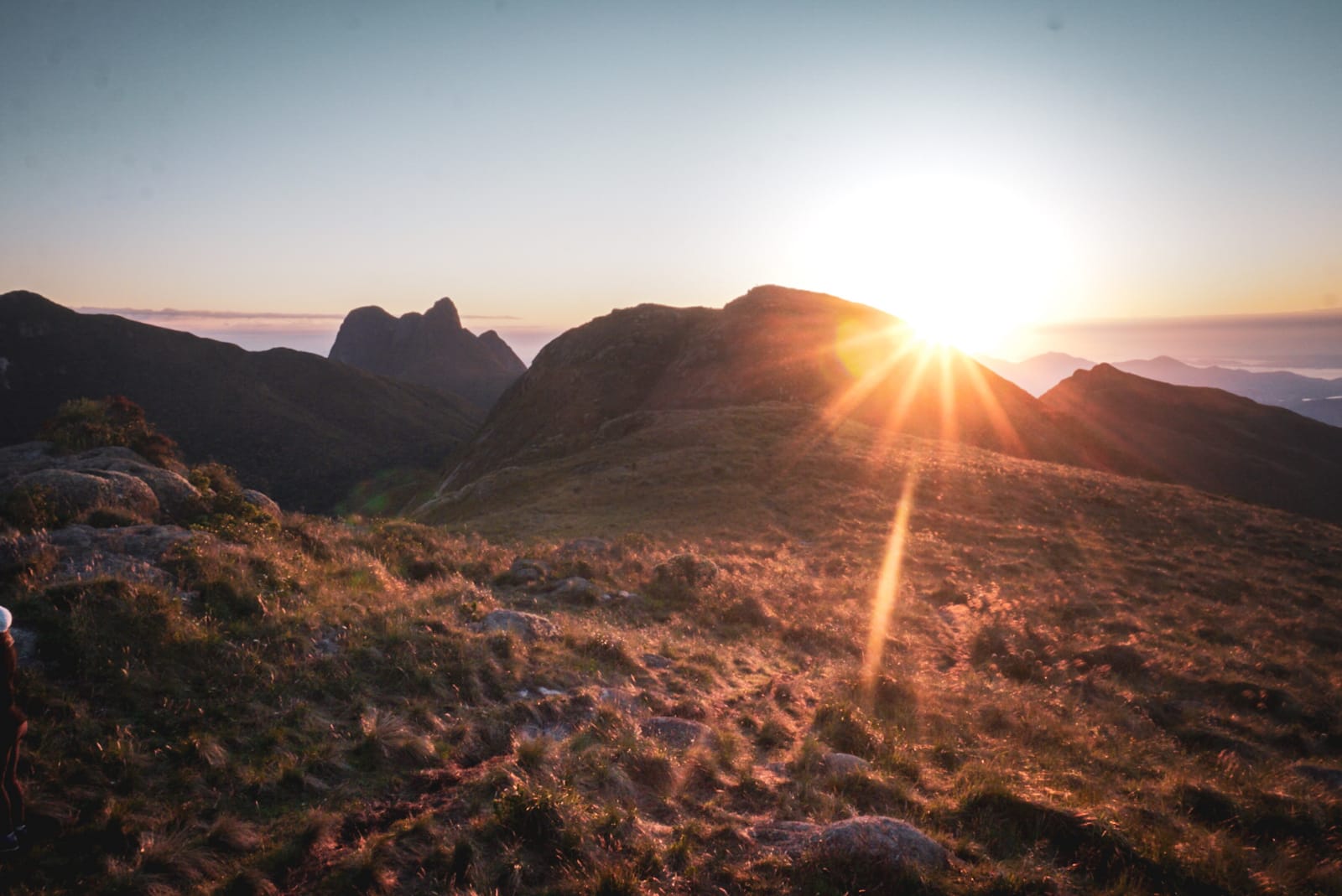 Sol nascendo por trás das montanhas, iluminando o campo com luz dourada