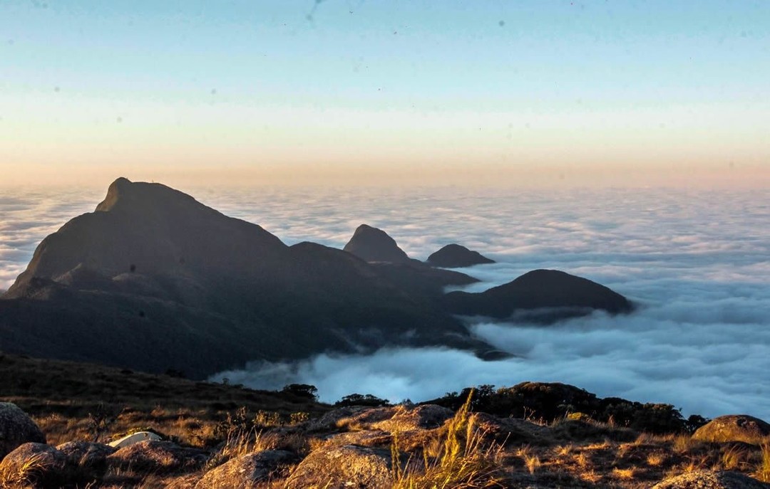Vista de montanhas cercadas por nuvens, parecendo um mar branco sob o céu claro